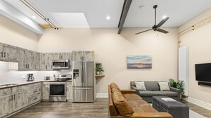A modern kitchen with stainless steel appliances, a dining area with a brown leather sofa, and a flat-screen TV mounted on the wall. - 124 Hurontario Unit 3 (Collingwood)