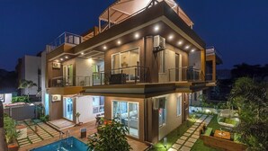 Ein modernes, zweistöckiges Haus mit Swimmingpool, Sitzgelegenheiten im Freien und einer überdachten Terrasse.