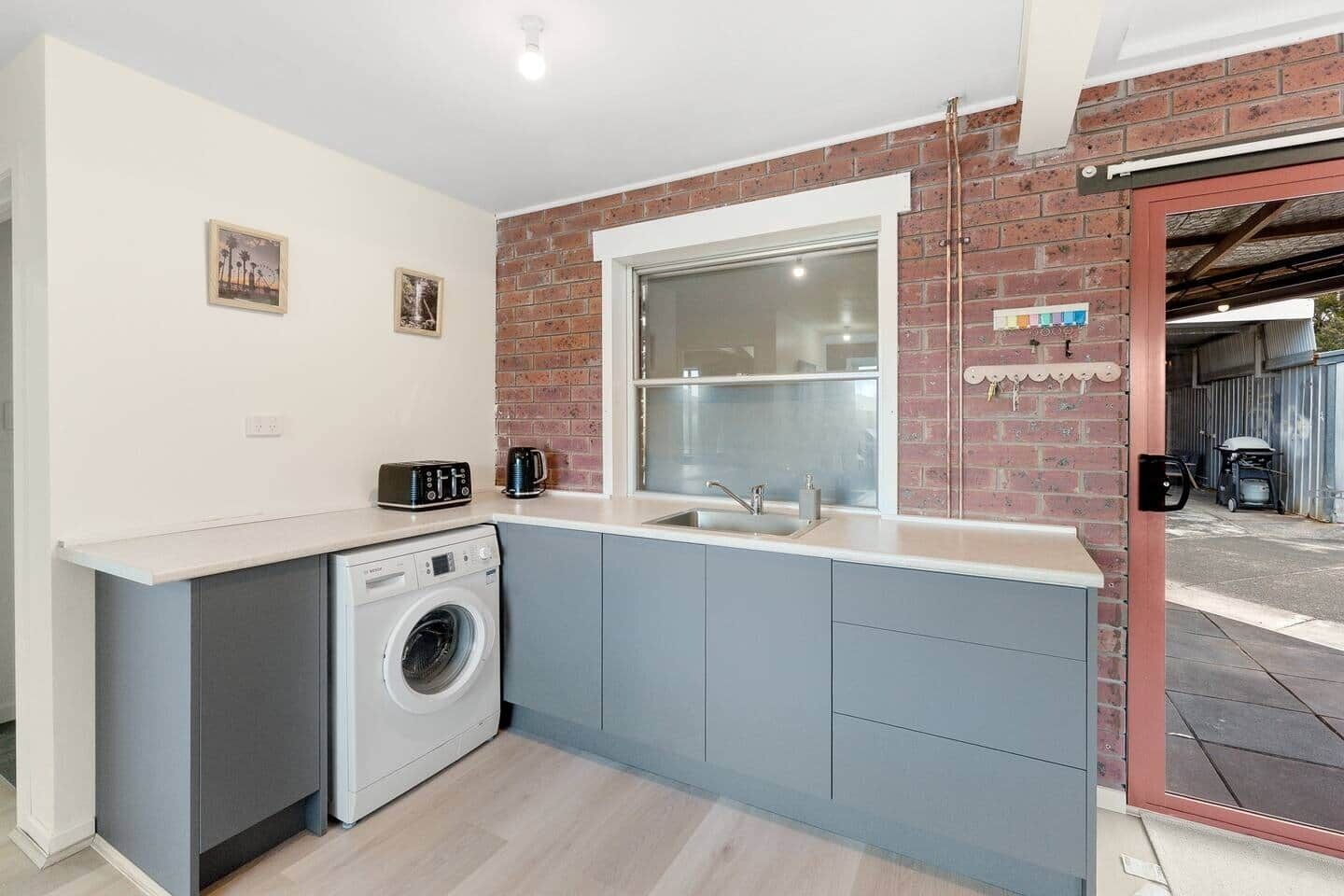 Een kleine keuken met een wasmachine, een spoelbak en een raam met uitzicht op een garage.
