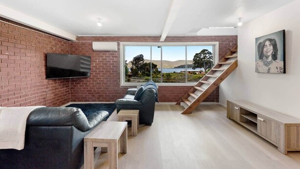 Ein modernes Wohnzimmer mit Backsteinwand, einem großen Fenster mit reizvollem Ausblick, einer Treppe und einem wandmontierten Fernseher.