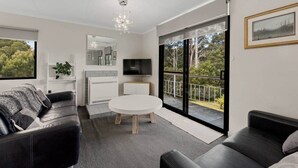 Ein modernes Wohnzimmer mit einem schwarzen Ledersofa, einem weißen runden Tisch und einem großen Fenster mit Balkon.
