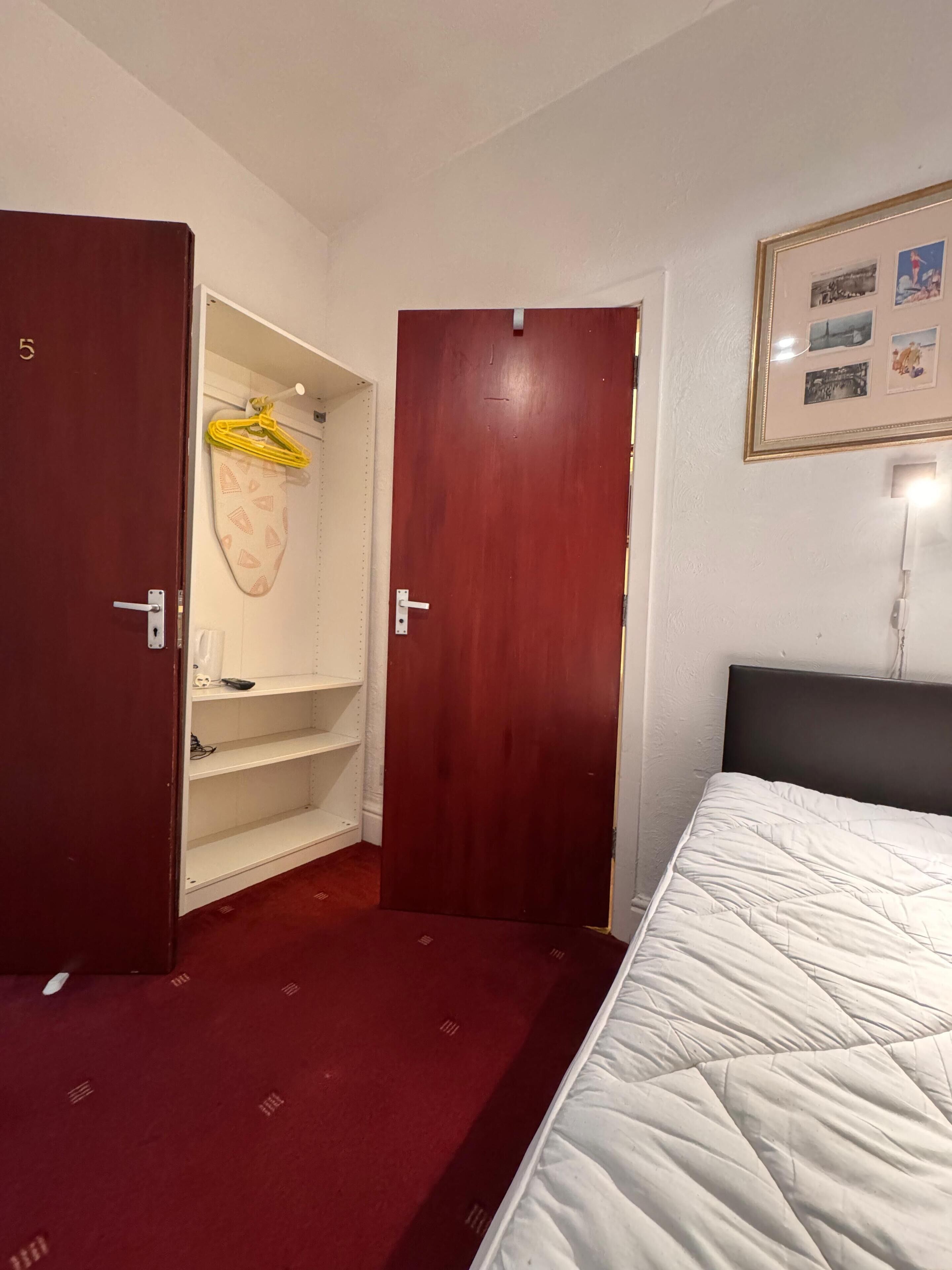 A hotel room with a bed, a wardrobe, and a shelf unit.