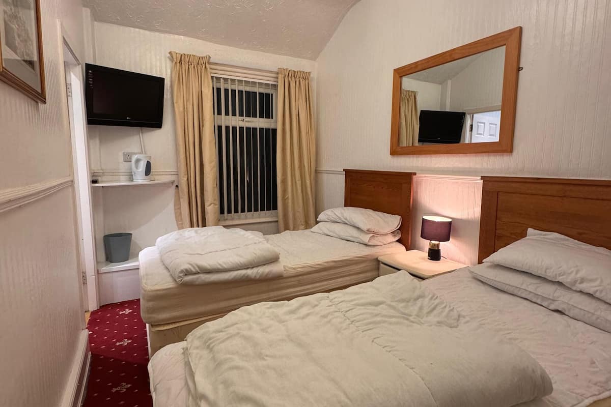 A hotel room with two beds, a television, a mirror, a chandelier, and a window with curtains.