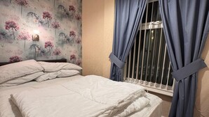 A neatly made bed with white linens, a floral wallpaper pattern on the wall, and a window with blue curtains. - No 34 Vance Road (Blackpool)