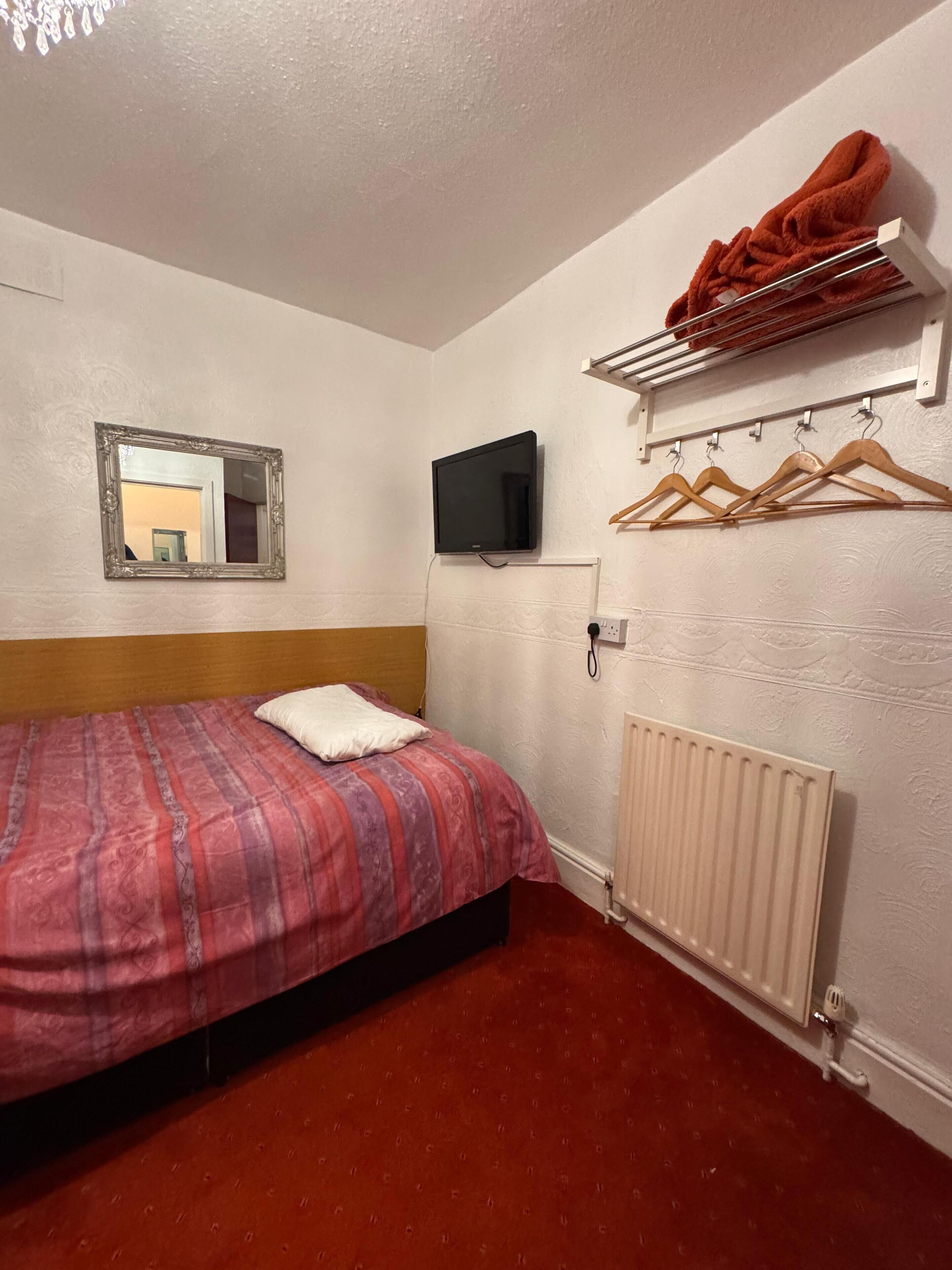 Habitación de hotel con cama, televisor, espejo y radiador.