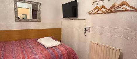Habitación de hotel con cama, televisor, espejo y radiador.