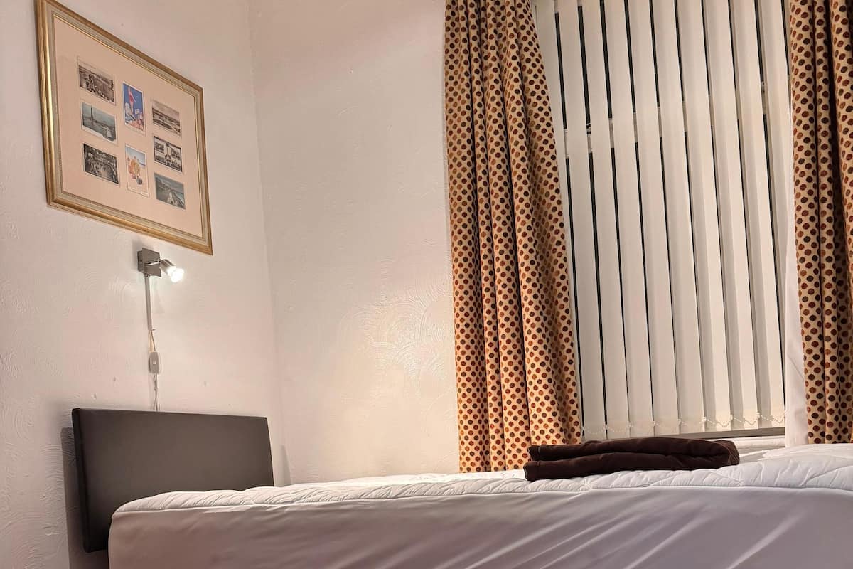 A hotel room with a bed, a headboard, a wall-mounted TV, a framed picture, and a window with curtains.