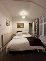 Een slaapkamer met een bed, nachtkastje, radiator, spiegel en een raam met zonwering.