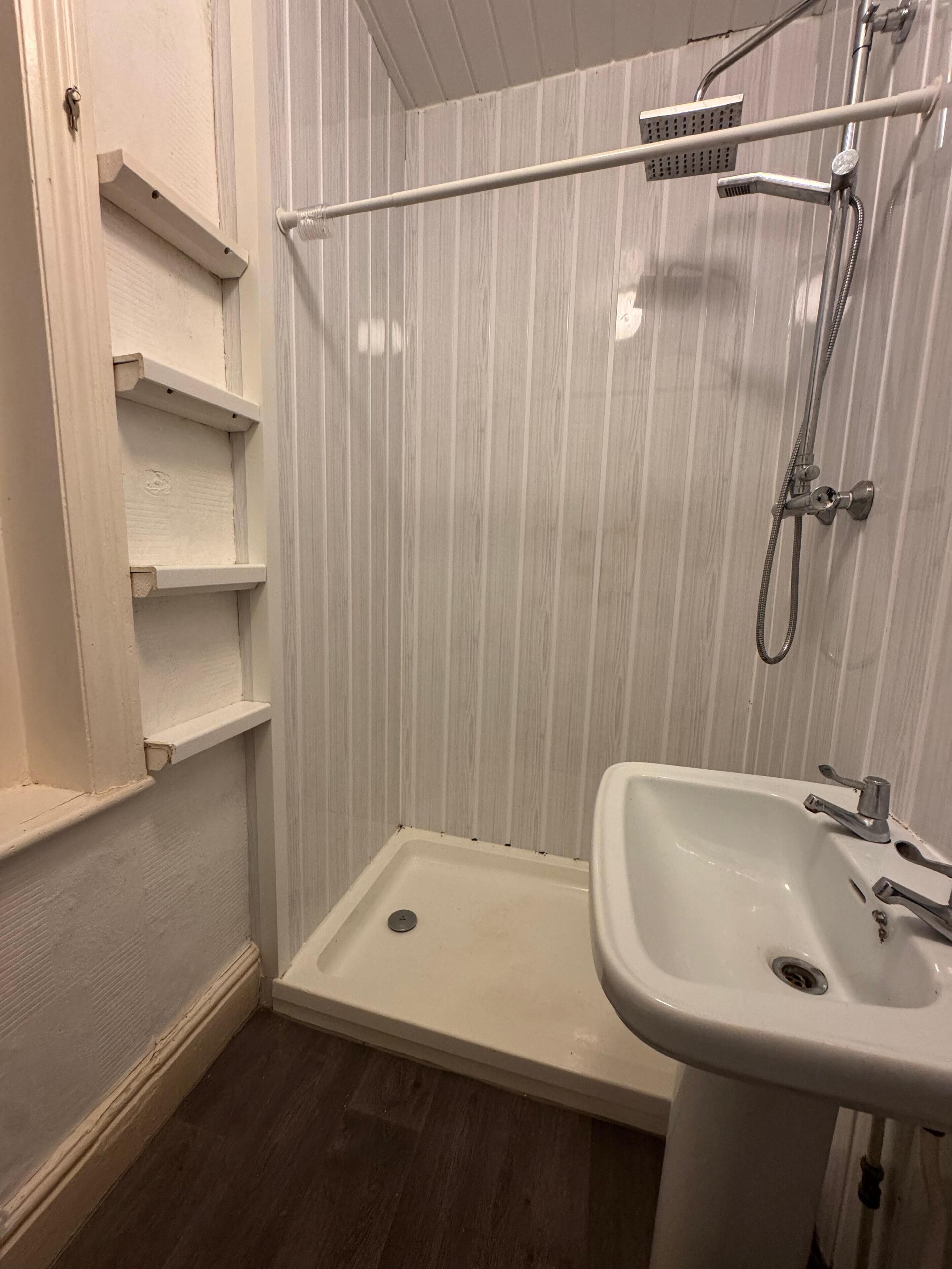 A bathroom with a shower, a sink, and built-in shelves.
