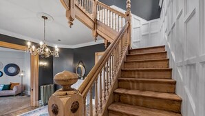 Una escalera de madera de diseño clásico que conduce a una habitación oscura con un candelabro y una mesa redonda.