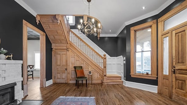 Una habitación amplia con una escalera de madera, un candelabro y un gran ventanal.