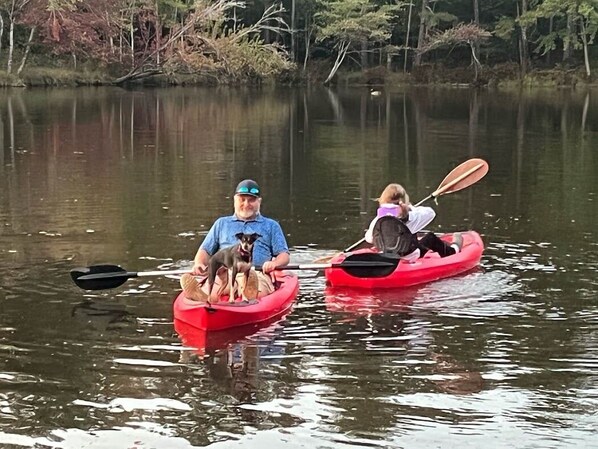 Two people in red kayaks on a calm lake with trees in the background.