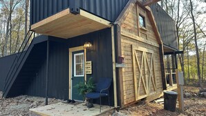 Une cabane rustique avec une façade en bois, une porte verte et une pancarte indiquant « Bienvenue ».