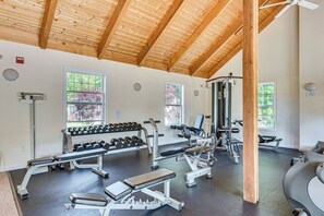 Une salle de sport équipée de divers appareils d’exercice, dotée de grandes fenêtres et d’un plafond en bois.