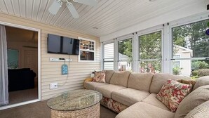A cozy living room with a beige sectional sofa, a glass coffee table, and a flat-screen TV mounted on the wall.