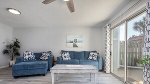 Una sala de estar con un sofá azul, una mesa de centro blanca y un cuadro en la pared.