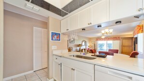 A kitchen with white cabinets, a large island with a sink, and a dining area with red chairs. - Paws Welcome at Ponce Landing 25 (St. Augustine)