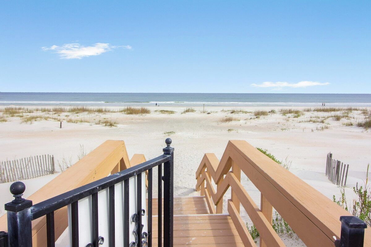A wooden boardwalk leading to a sandy beach with a clear sky.