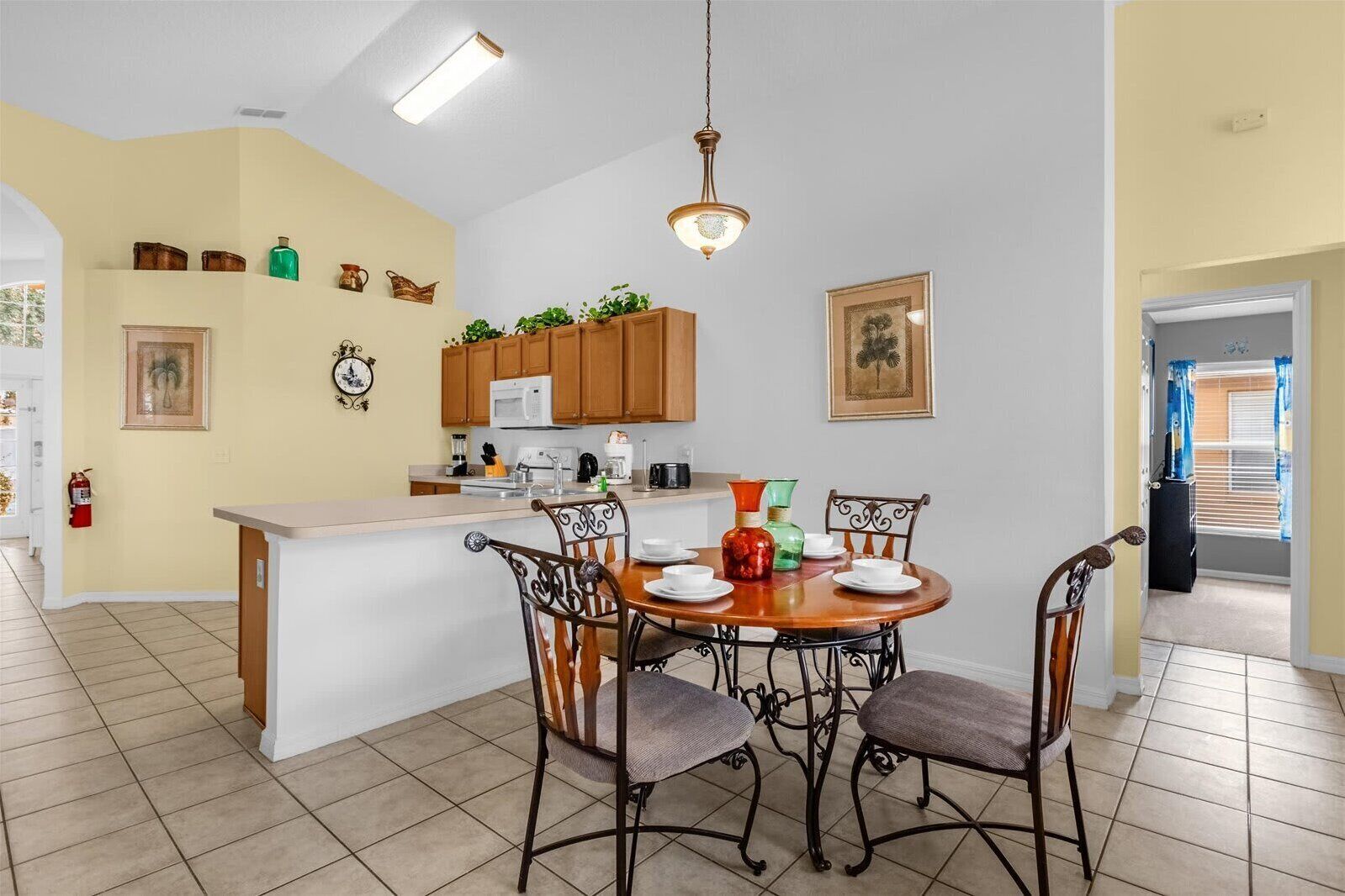 A dining area with a round table, four chairs, a kitchen with wooden cabinets, and a white countertop.