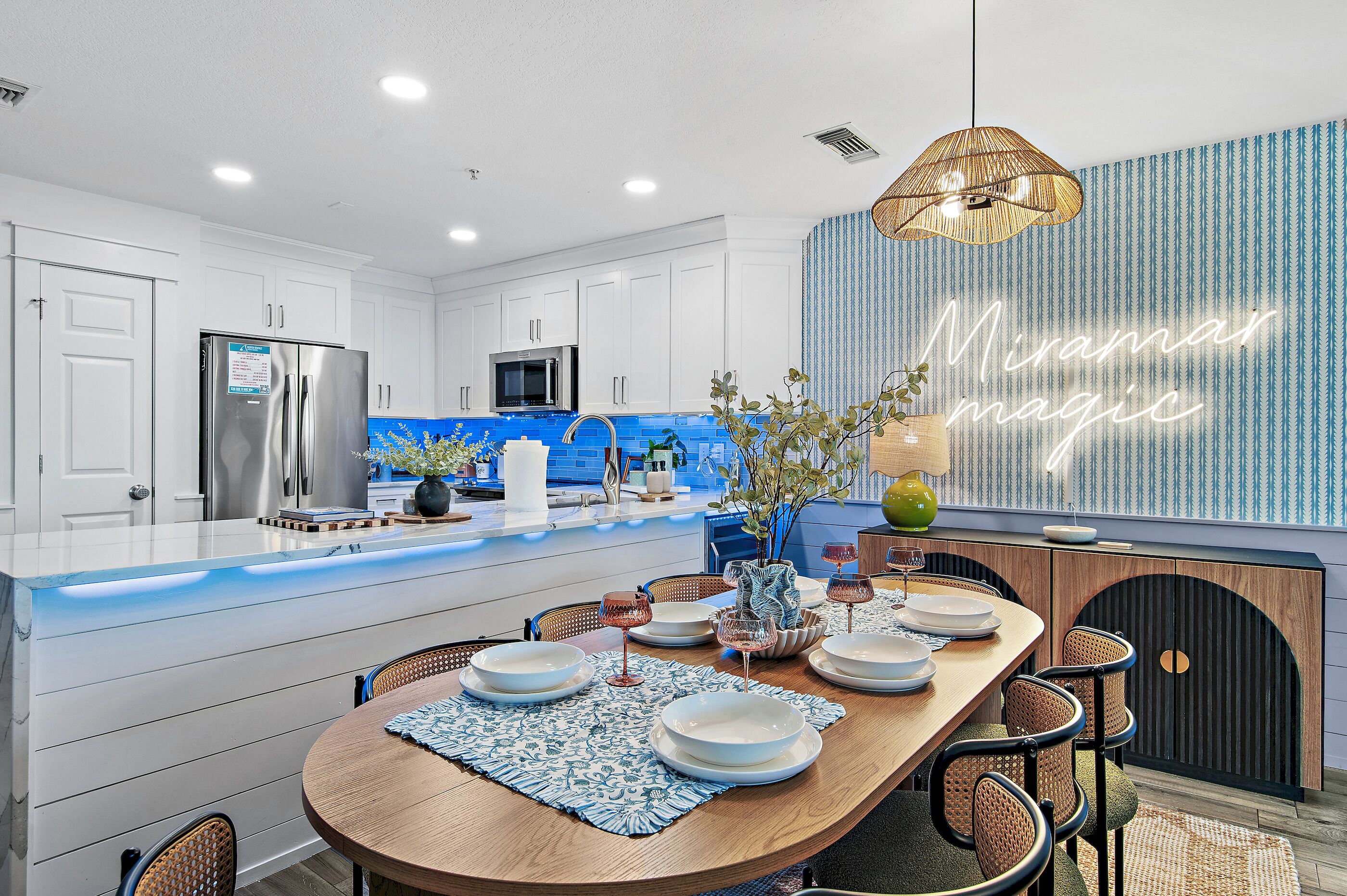 A modern kitchen with white cabinetry, a blue backsplash, and a dining area with a wooden table set for four.