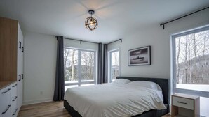 Ein Schlafzimmer mit einem großen Bett, einem Nachttisch, einem Kleiderschrank und einem Fenster mit Blick auf Bäume.