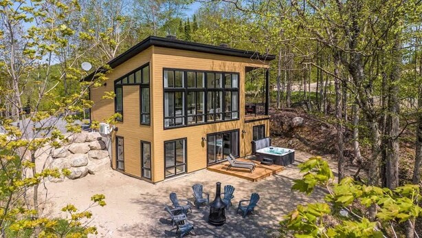 Ein modernes, zweistöckiges Haus mit großen Fenstern, einer Terrasse und Sitzgelegenheiten im Freien.