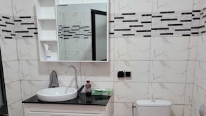 A bathroom with a white sink, mirror, and toilet. There are cabinets below the sink and a trash can next to the toilet. The floor has a patterned tile design.