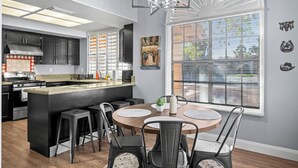 A modern kitchen with a central island, black cabinets, and a dining area with a round table and chairs.