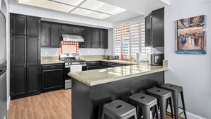 A modern kitchen with dark cabinets, a central island with stools, a stove, and a microwave.