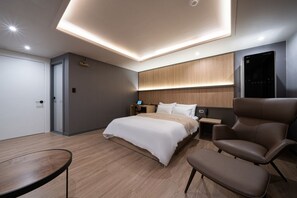 Una habitación de hotel moderna con una cama grande, un área de descanso con una silla y una mesa, y un televisor integrado.