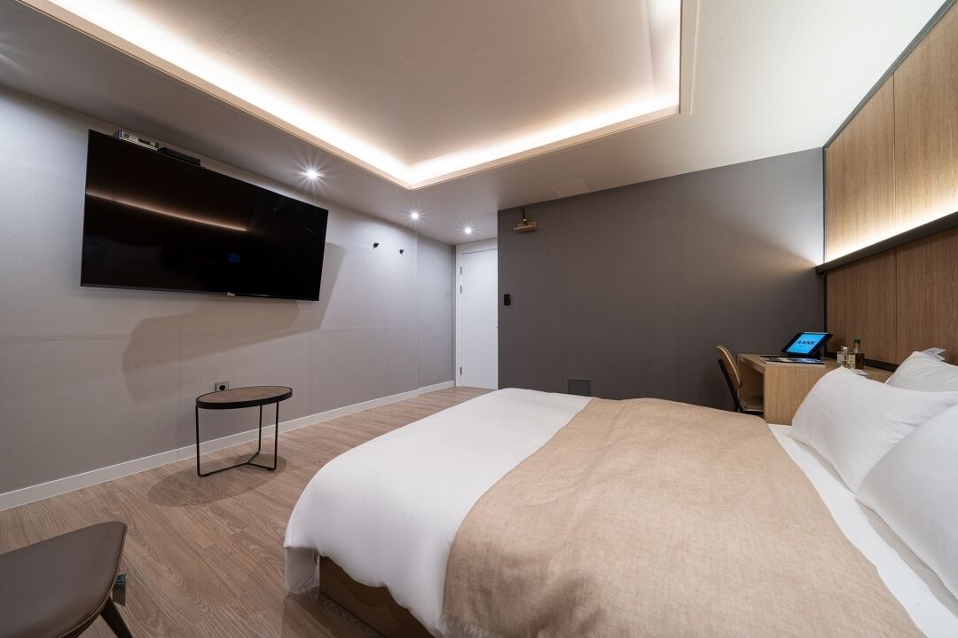 Una camera d'albergo moderna con un letto grande, una TV fissata al muro, una scrivania con un portatile e un piccolo tavolino rotondo.