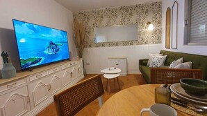 A living room with a television, a green sofa, a dining table with chairs, and a small white cabinet. - Charming apartment in Vigo with views of the valley (pet friendly) (Vigo)