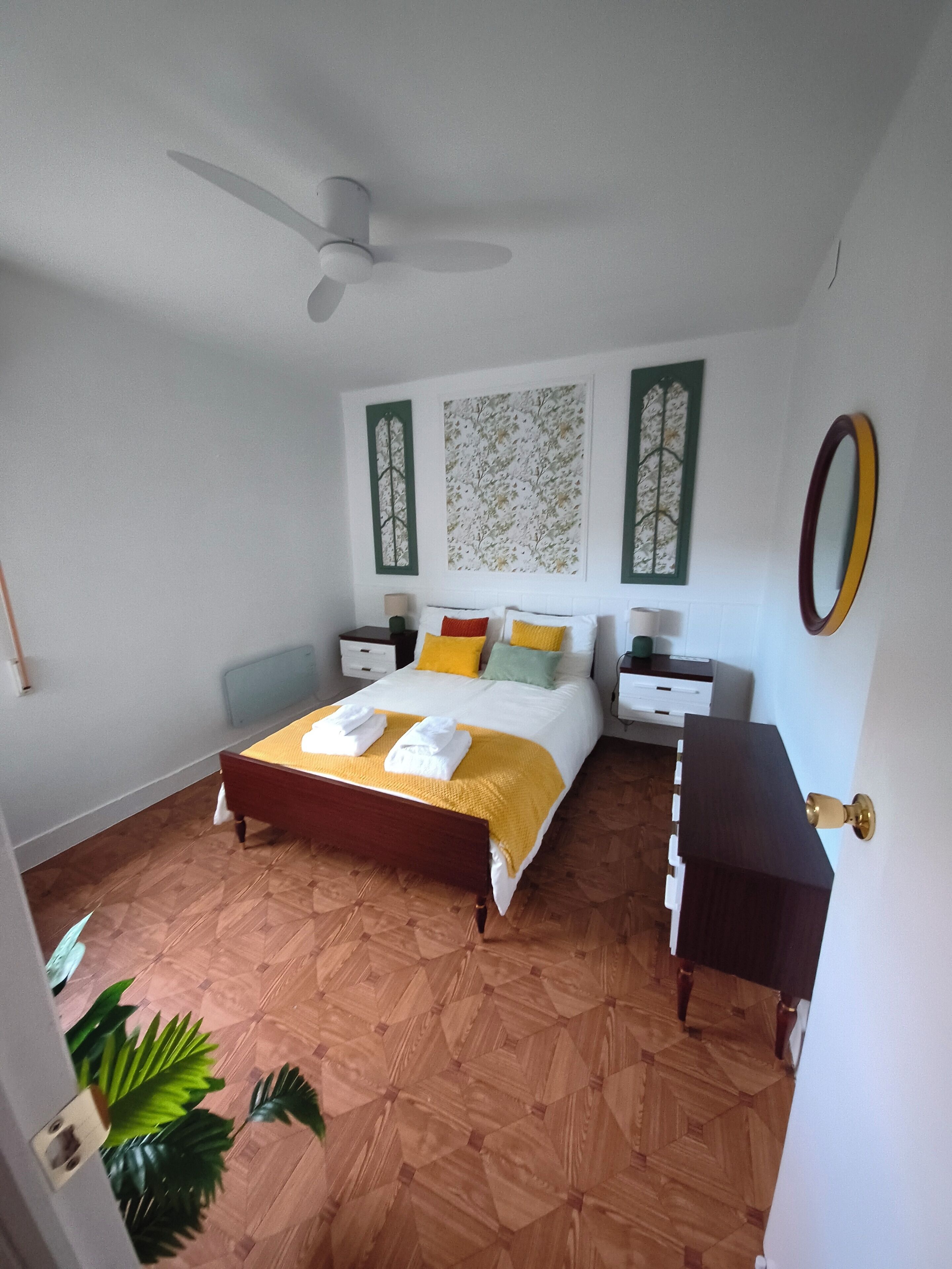 Une chambre à coucher comprenant un lit, des tables de chevet, une commode, un ventilateur de plafond et un grand miroir.