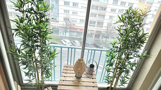 Ein Balkon mit zwei Holzstühlen, einem kleinen Tisch und zwei Kübelpflanzen.