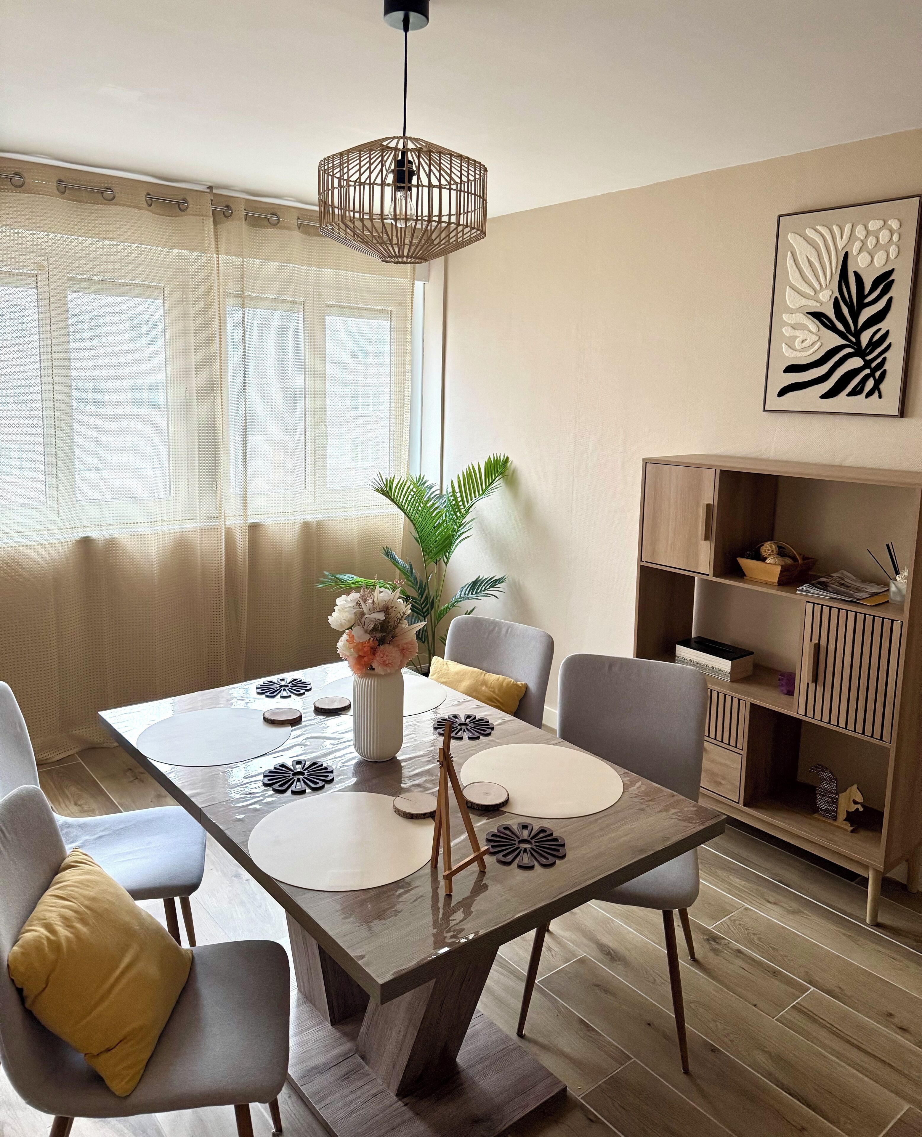 Een eetgedeelte met een houten tafel, stoelen, een vaas met bloemen en een hanglamp.