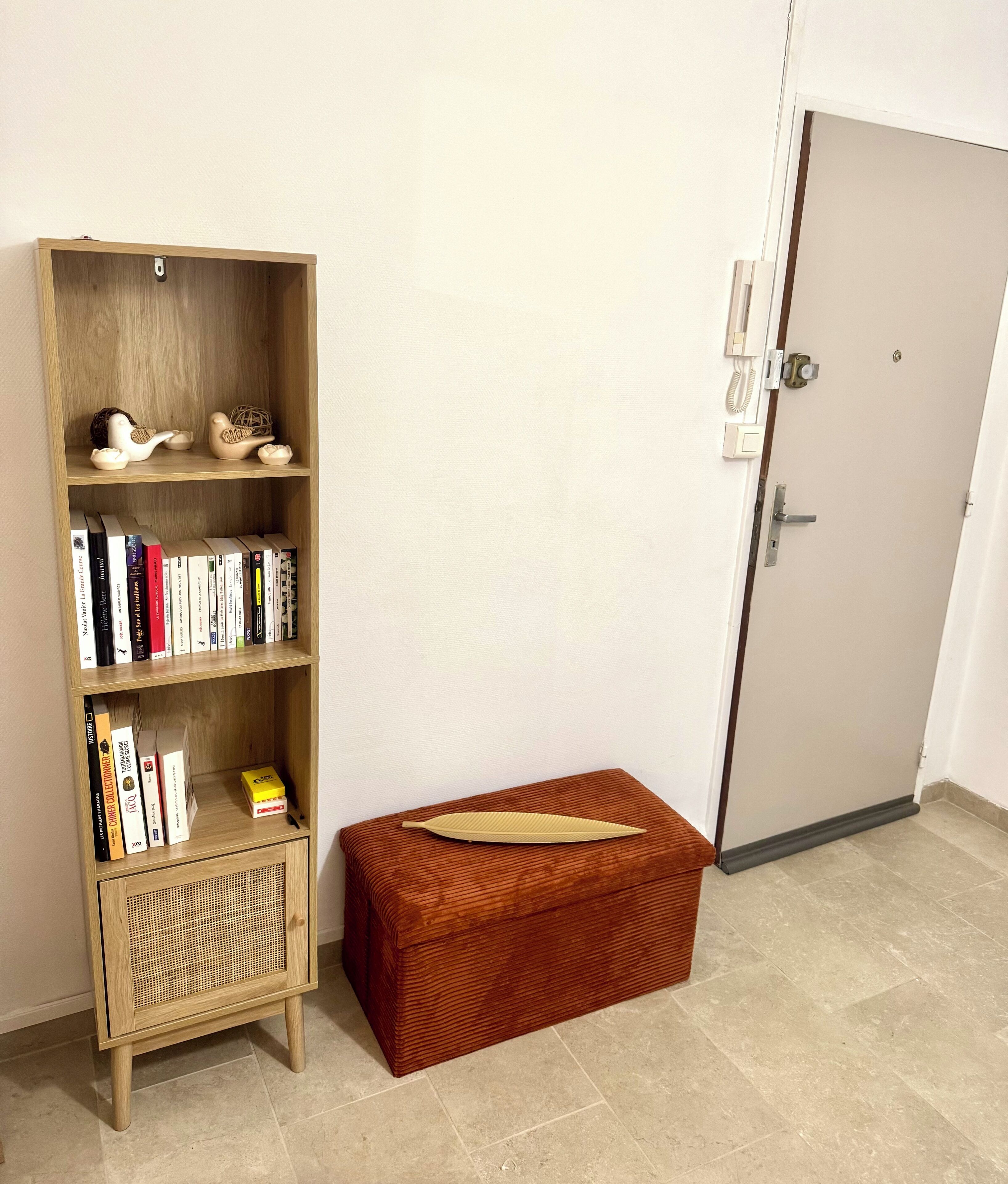 Una habitación con una estantería de madera, un pequeño cofre de madera y una puerta.