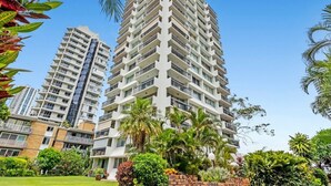 A high-rise residential building with multiple balconies, surrounded by lush greenery and palm trees. - 12th Floor Riverfront Retreat Views Walk to Beach (Surfers Paradise)