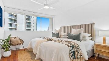 A modern bedroom with two beds, a ceiling fan, a large window, and a view of buildings.