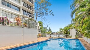 A swimming pool with a tiled edge, surrounded by a white fence and palm trees. - 12th Floor Riverfront Retreat Views Walk to Beach (Surfers Paradise)