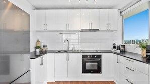 A modern kitchen with white cabinets, a black countertop, a stainless steel sink, and an oven. - 12th Floor Riverfront Retreat Views Walk to Beach (Surfers Paradise)