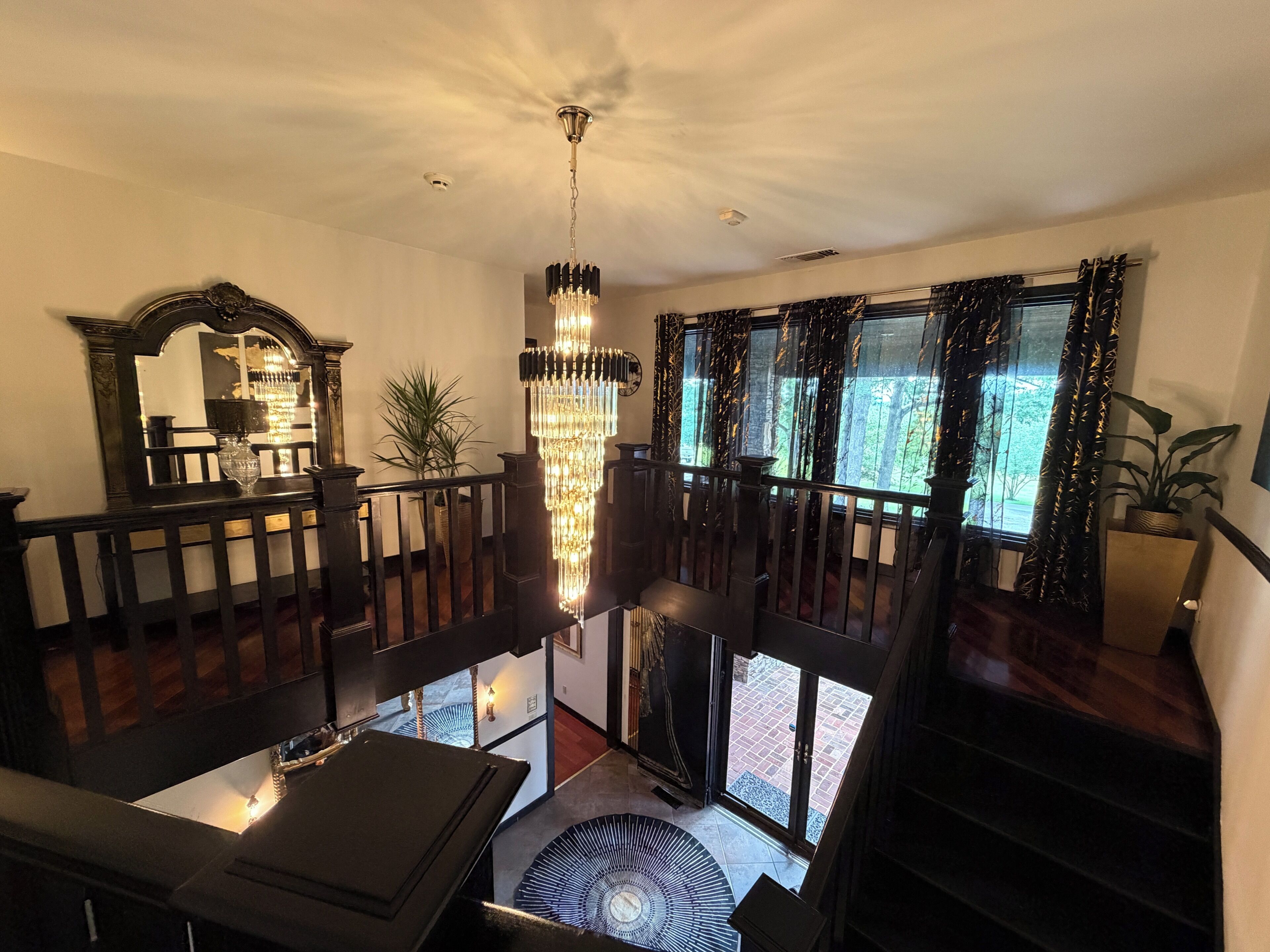 A grand staircase with a chandelier, a mirror, and a view of the outdoors.