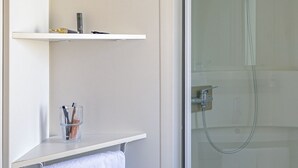 A bathroom with a glass-enclosed shower, a white towel hanging on a rack, and a shelf with a towel and a glass of water. - Waterfront mobile home (Saint-Florent)