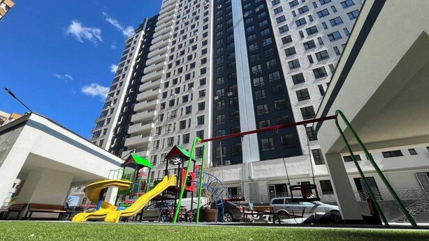 Un terrain de jeux avec des toboggans et une grande roue, entouré de grands immeubles d’habitation.