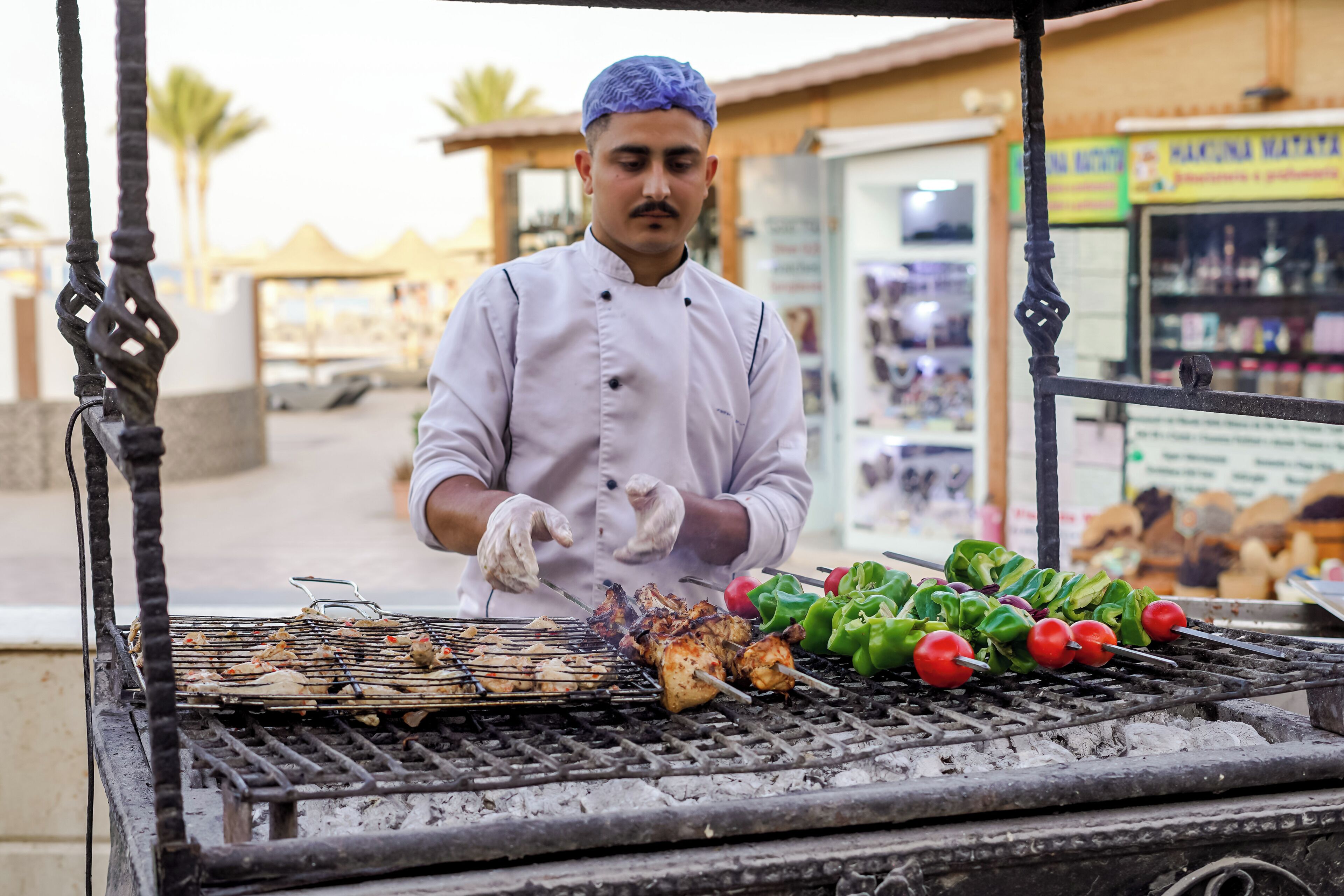 A street food vendor grilling meat and vegetables on an outdoor grill.