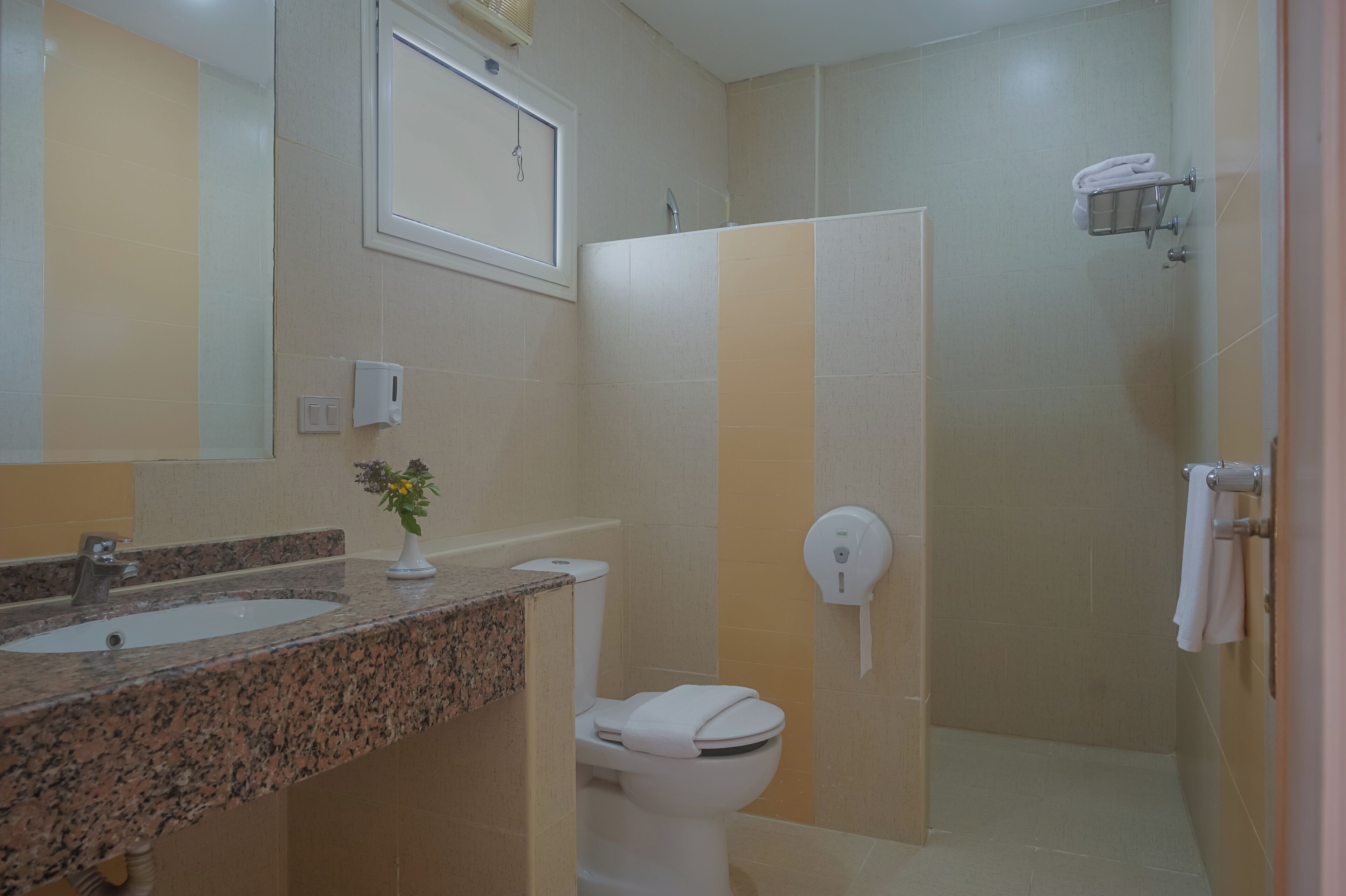 A bathroom with a granite countertop, a toilet, a shower stall, and a towel rack.