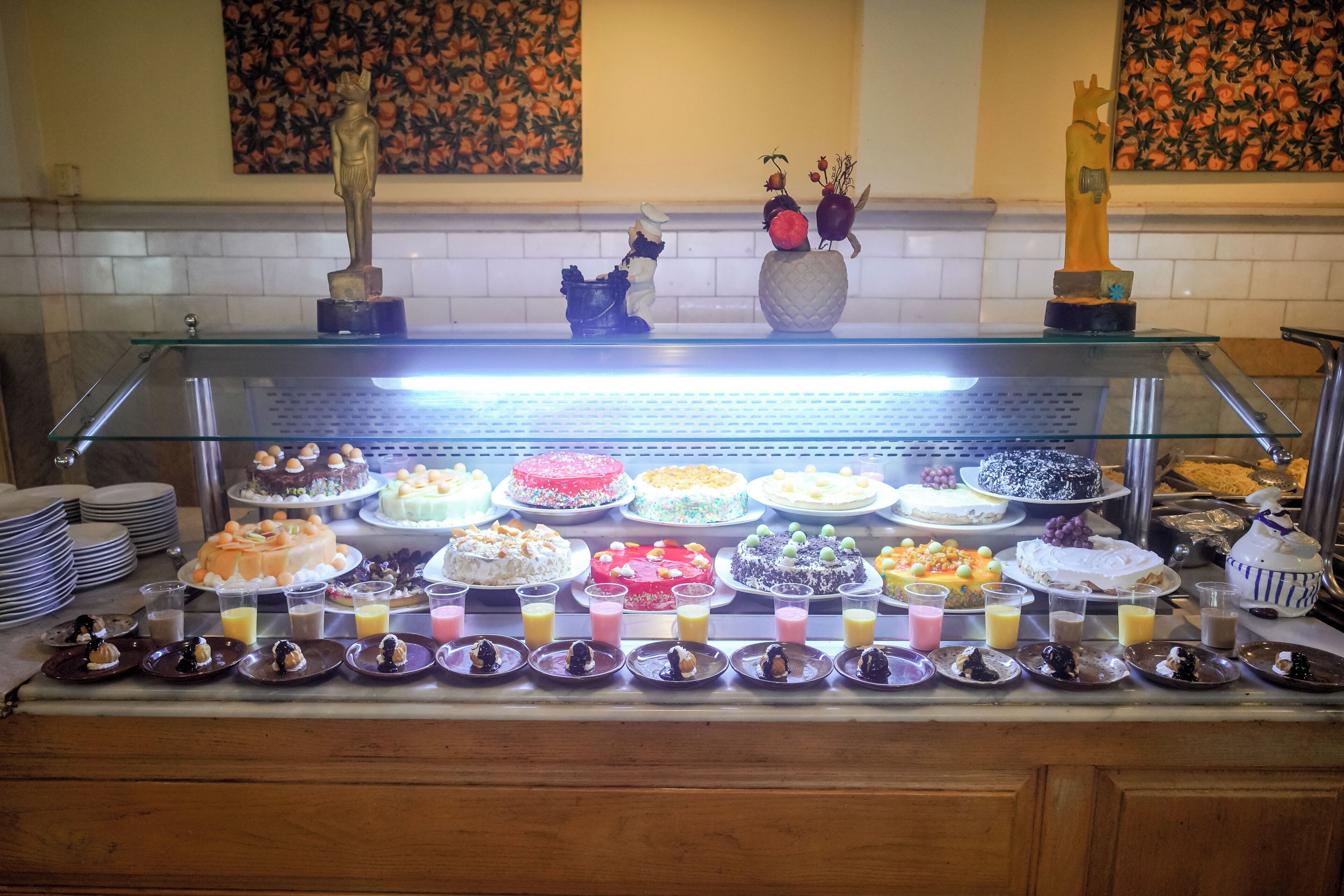 Zona de bufé con varios pasteles y postres expuestos en un mostrador de vidrio.