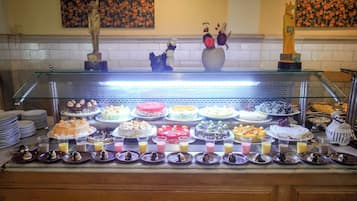 Zona de bufé con varios pasteles y postres expuestos en un mostrador de vidrio.