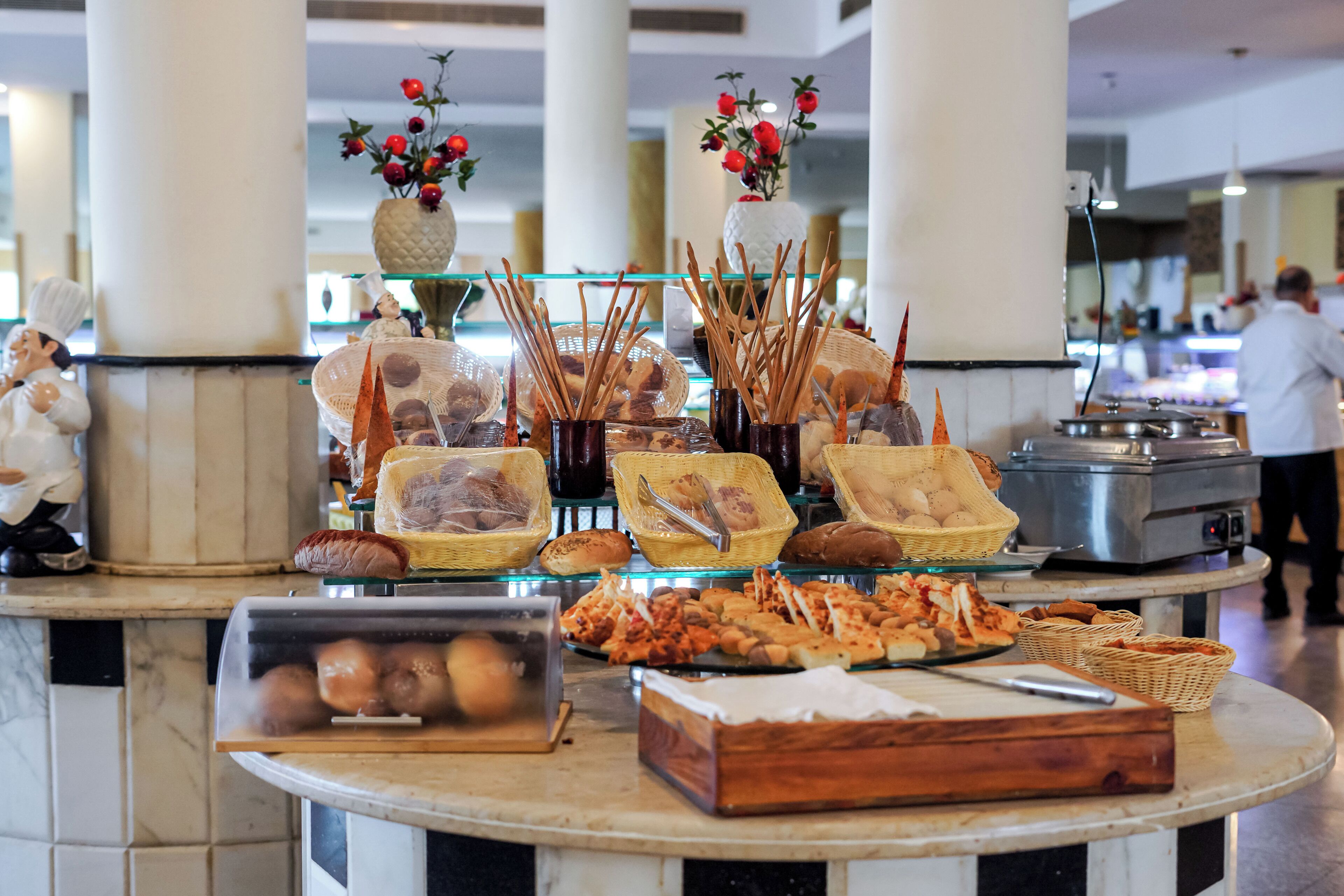 A buffet setup with various food items and utensils, including bread, pastries, and a display case with eggs.