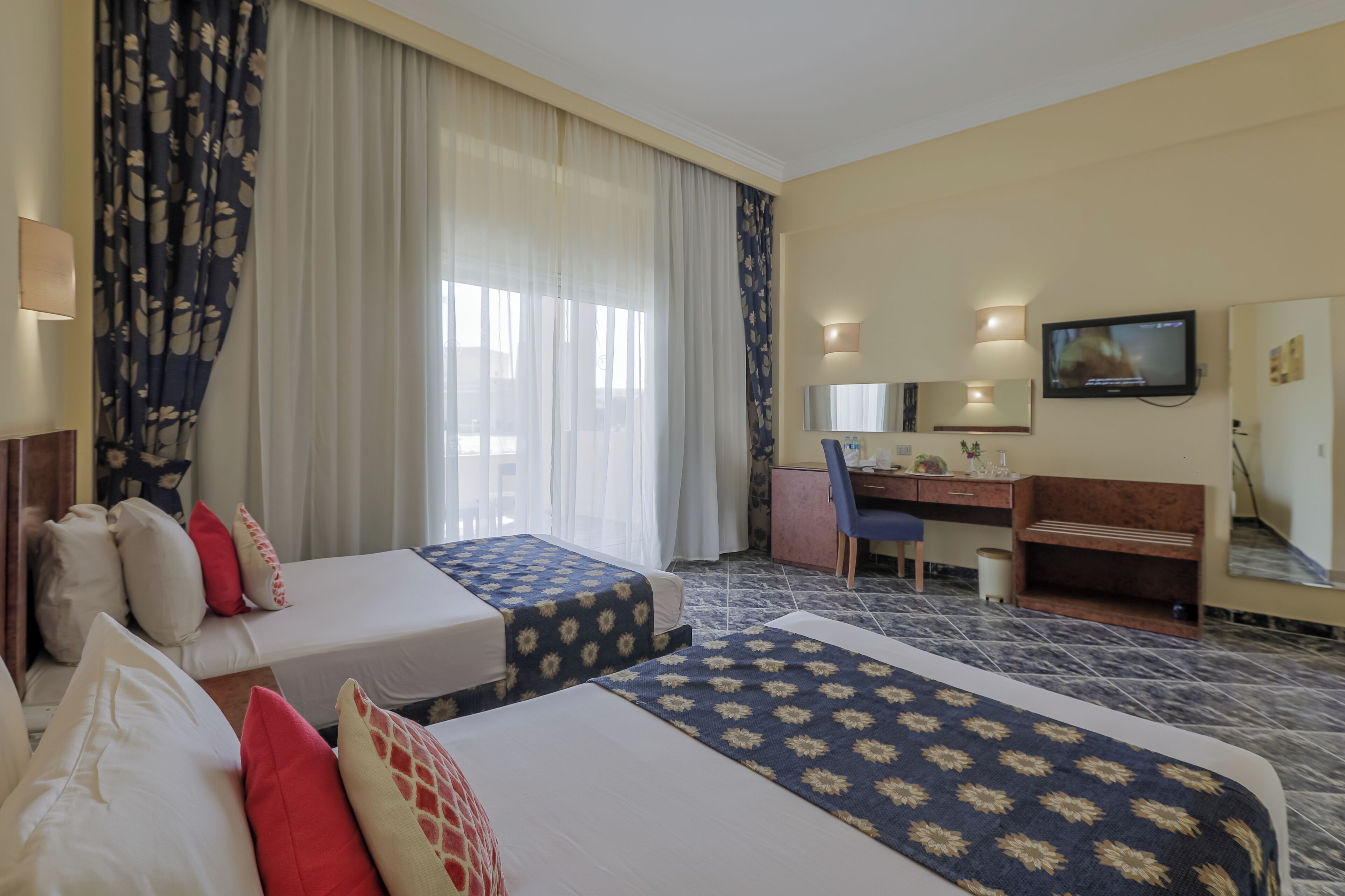 A hotel room with two beds, a desk, a chair, a television, and a bathroom.
