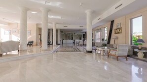 Un hall d’entrée spacieux, doté d’un sol en marbre, de grandes colonnes blanches et d’un comptoir d’accueil.